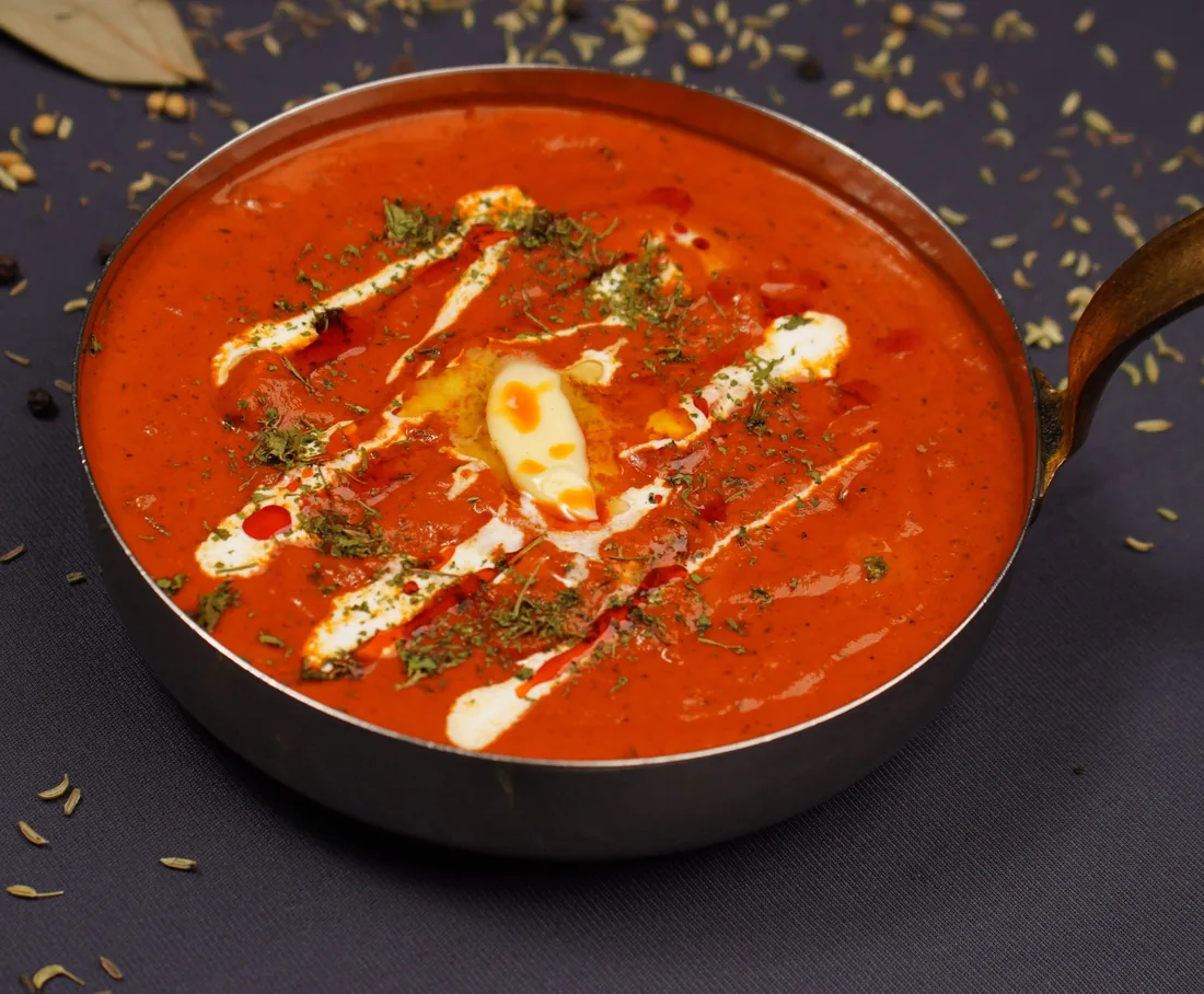 Creamy masala curry finished with cream and herbs in a brass-handled pan